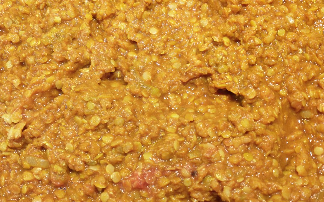 Image shows a pan of the red lentil curry described in this recipe. The lentils appear as red-yellow dots on a darker background of the same hue.