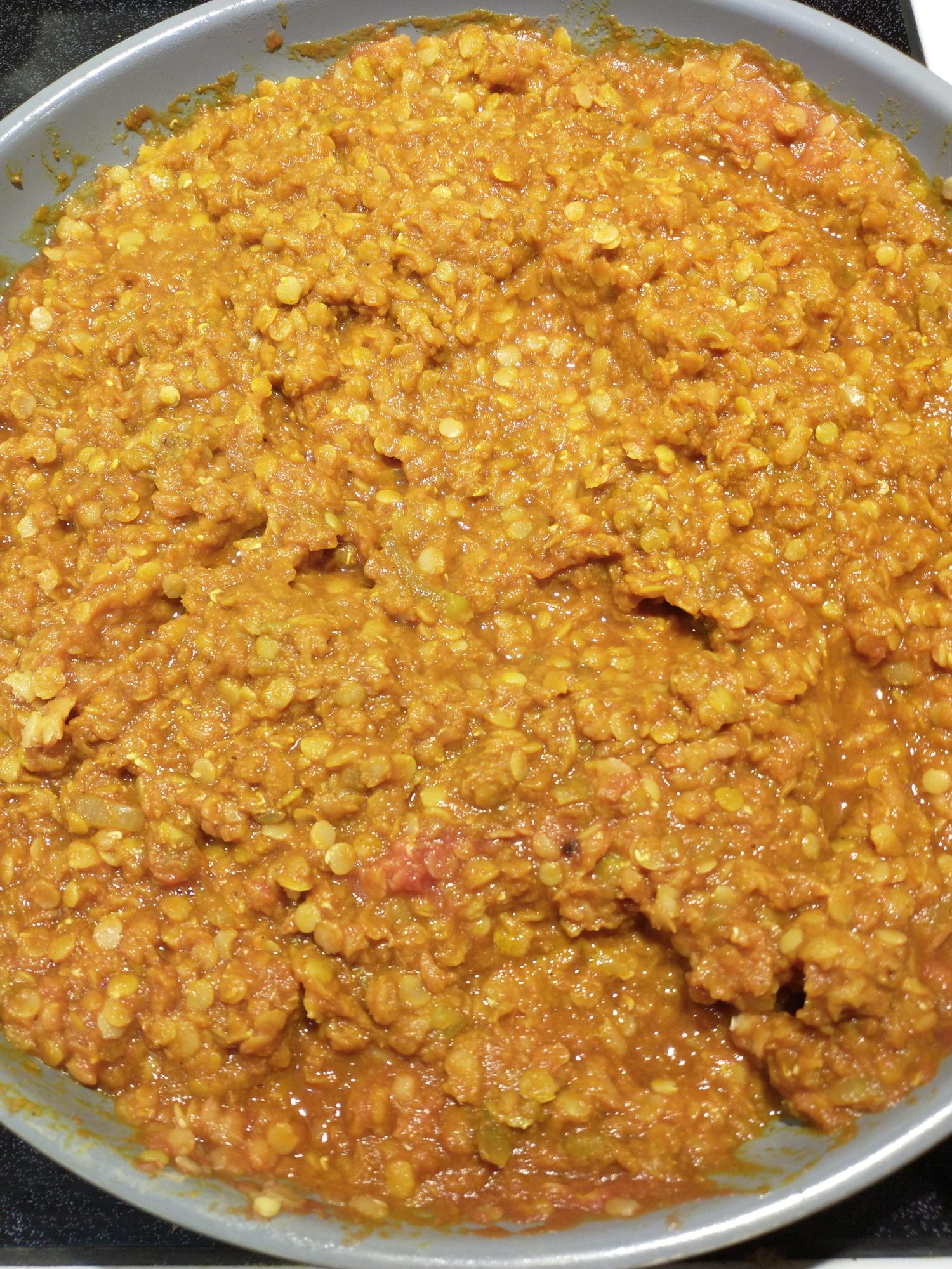 Image shows a pan of the red lentil curry described in this recipe. The lentils appear as red-yellow dots on a darker background of the same hue.