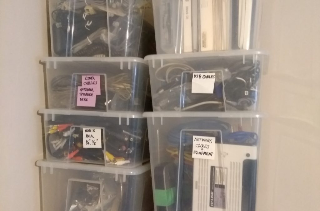 A stack of clear plastic bins, each containing various computer and electronics components. Each bin has a label describing the contents.