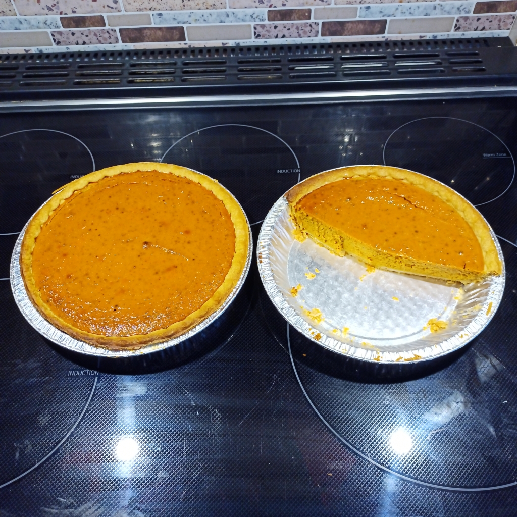 Two pies on a black stove-top. One of the pies is slightly more than half eaten. Yum.